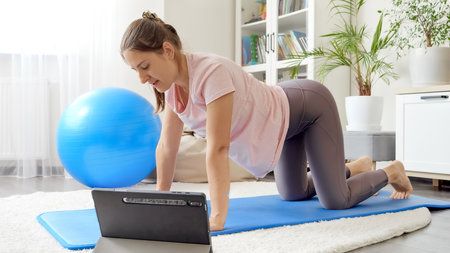 Young woman doing fitness at home using tablet computer.の写真素材