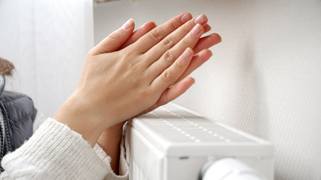 Closeup of woman feeling col warming her hands at wall heater.