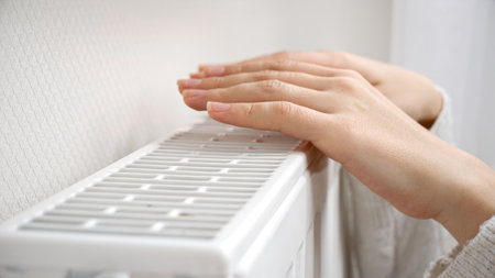 Closeup of female hands warming over the wall radiator at home.の写真素材