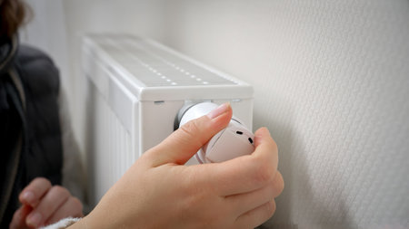 Closeup of woman adjusting heating radiator thermostat and warming her hands. Concept of energy crisis, high bills, broken heating system, economy and saving money on monthly utility paymentsの写真素材