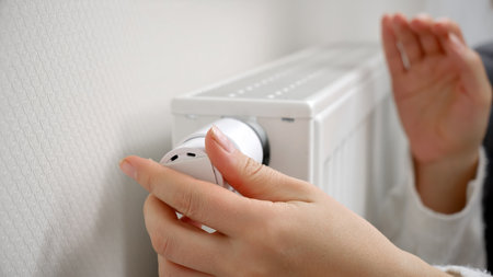 Closeup of woman adjusting heating radiator valve and warming hands. Concept of energy crisis, high bills, broken heating system, economy and saving money on monthly utility paymentsの写真素材