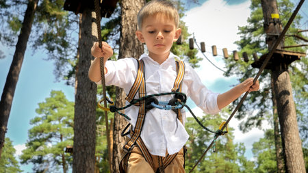 Portrait of little boy smiling while walking over strung rope in climbing training center. Active childhood, healthy lifestyle, kids playing outdoors, children in natureの写真素材