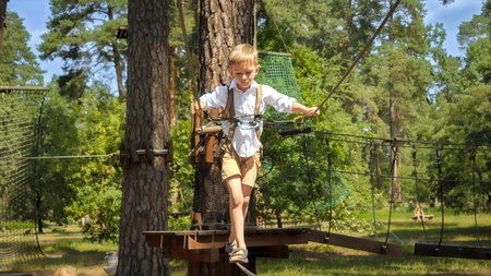 Boy holding by rope while walking on cable between two trees. Active childhood, healthy lifestyle, kids playing outdoors, children in natureの写真素材