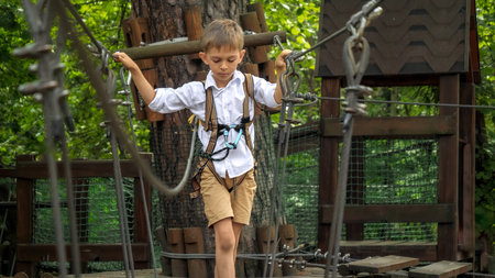 Cute boy having fun while walking on wobbly rope bridge at adventure park. Active childhood, healthy lifestyle, kids playing outdoors, children in natureの写真素材