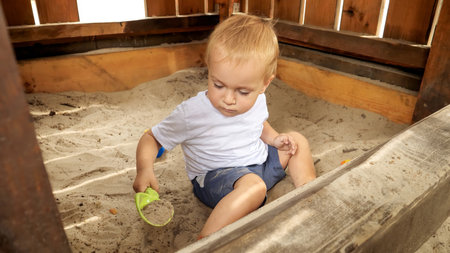 Cute little boy digging sand with toy shovel in sandbox at park. Kids playing outdoors, children having fun, summer vacation and holidayの写真素材