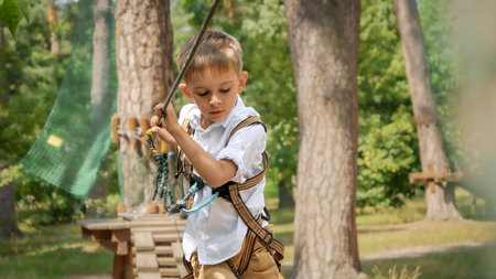 Portrait of little boy having fun and extreme adventure at rope park in summer camp. Active childhood, healthy lifestyle, kids playing outdoors, children in natureの写真素材