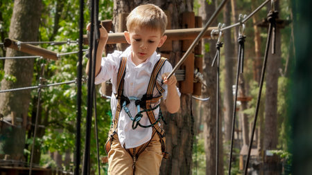 Portrait of little boy crossing obstacles at outdoor climbing training park. Active childhood, healthy lifestyle, kids playing outdoors, children in natureの写真素材