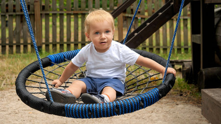 Cute smiling toddler boy swinging in rope nest swing at park.の写真素材