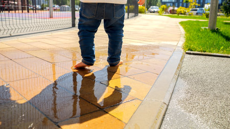 Closeup of barefoot baby boy walking in the water puddle on street at sunny summer day. Kids outdoors, children in nature, baby playing outsideの写真素材