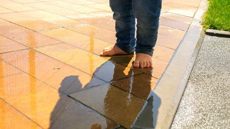 Closeup of barefoot baby walking over puddle and splashing water. Kids outdoors, children in nature,...