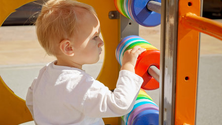 Portrait of blonde baby boy playing on colorful wooden playground outdoors. Children developments, kids education, baby learningの写真素材