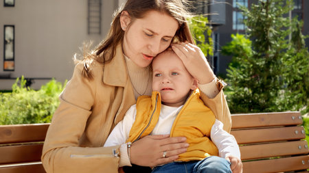 Little toddler boy sitting on mothers legs in park and crying.の写真素材