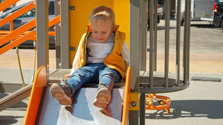 Little baby boy sitting on the top of the slide at playground and asking for help. Happy parenting, family having time together, kids and parents outdoorsの写真素材