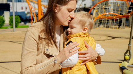 Young mother consoling and hugging her upset baby boy on playground. Children playing outdoor, kids outside, summer holiday and vacationの写真素材