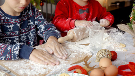 Closeup of child's hands rolling dough for Christmas cookies for Santa on kitchen table.の写真素材