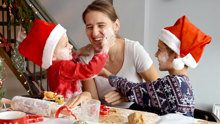 Two cheerful boys playing with mother and throwing flour in her while cooking on kitchen on Christmas.の写真素材