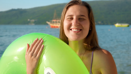 Portrait of smiling brunette woman in bikini posing on beach before swimming in sea with inflatable swimming ring.の写真素材