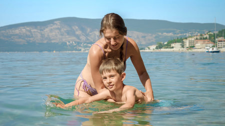 Young woman holding her son learning swimming on the sea beach on summer holidays.の写真素材