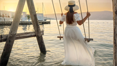 Woman in an elegant long dress enjoys a sway under the setting sun. Tourism, the tranquility of summertime, freedom, and the adventure of travelの写真素材