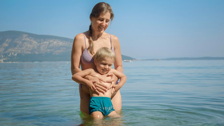 happy cheerful toddler boy laughing and mother throwing him and catching on the sea beach.の写真素材