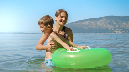 Young caring mother helping her little son getting inside the inflatable swimming ring in the sea. Family holiday, vacation and fun summertime of children and parentsの写真素材