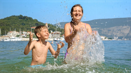 Mother and her son playing and splashing water at the sea beach. Family holiday, vacation memories, and the pure joy of summertime.の写真素材