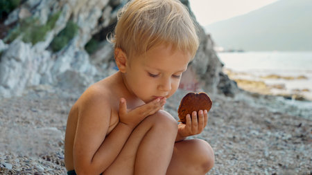 Little toddler boy sitting on the sea beach and eating pancakes.の写真素材