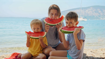 Portrait of happy family enjoying eating watermelon on the sea beach. Summertime, holiday, vacation, happiness and relaxationの写真素材