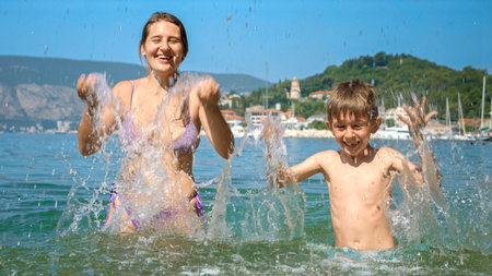 Cheerful woman with son enjoying summer beach vacation splashing sea water.の写真素材