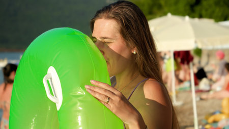 Young woman in bikini blowing air and inflating swimming ring on beach at summer holiday resort.の写真素材