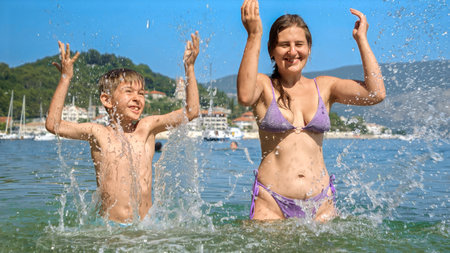 Cheerful mother and her son playfully splash in the ocean waves at the beach, creating cherished family holiday memories.の写真素材