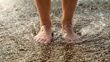 Closeup of warm sea water flowing between female legs standing on an ocean beach.の写真素材