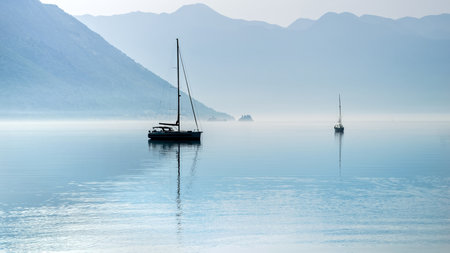 Silhouette of two yachts moored in calm sea harbour with rising morning mist and fog.の写真素材