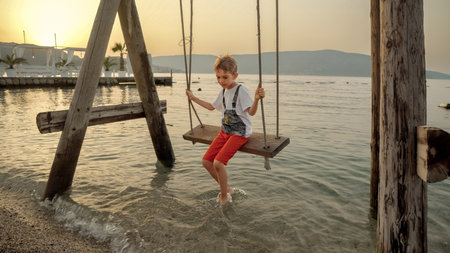 Little boy enjoying riding on swing at the sea beach. Holiday, summer vacation and tourism.の写真素材