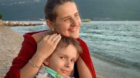Young loving mother hugging her little son covering in beach towel and feeling cold at sea. Holiday, summer vacation and tourism.の写真素材