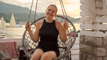 Happy smiling woman enjoying swinging in swing on the sea beach at sunset light.の写真素材
