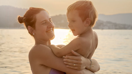 Silhouette of happy smiling woman holding her little baby son against sunset light over the sea.の写真素材