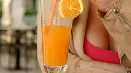 Closeup of woman stirring ice in glass of fresh orange juice while sitting in restaurant.の写真素材