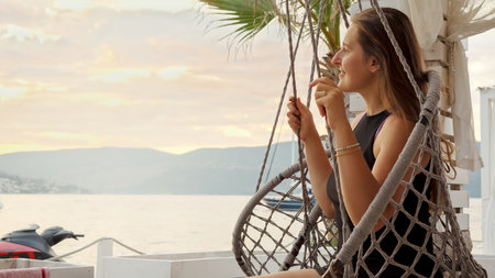 Smiling young woman with long hair enjoying sunset and swinging on the beach. Concept of summertime, vacation and beach holidaysの写真素材