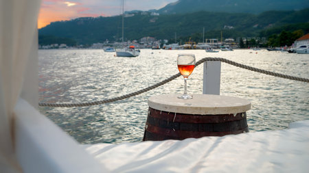 Glass of rose wine standing on wooden table at the beachfront bar against calm sea waves and sunset sky.の写真素材