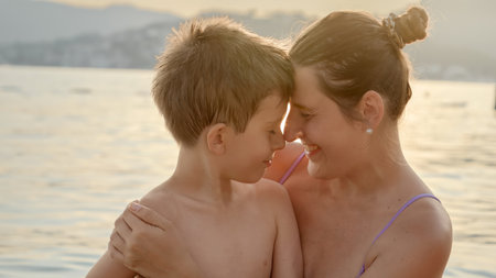 Portrait of smiling boy hugging and having fun with his mother on sea beach at sunset. Holiday, summer vacation and tourism.の写真素材