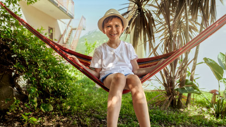 Joyful memories: Little boy in hat enjoys garden hammock, embodying carefree vacation.