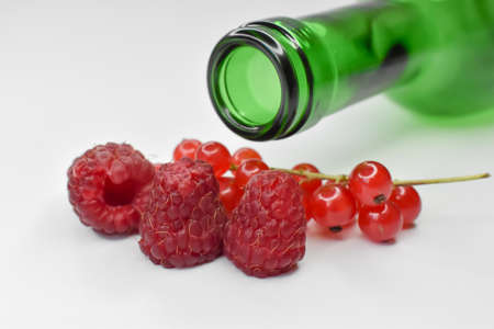 Fresh raspberries and currants with a green bottle.