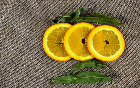 Slices of orange with green leaves on a burlap backgroundの写真素材