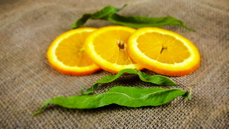 Slices of fresh orange with green leaves on sackcloth backgroundの写真素材