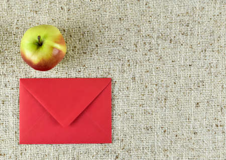 Red envelope and apple on sackcloth background, top view. Space for textの写真素材
