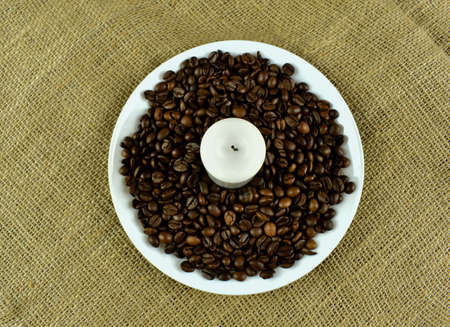 Coffee beans on a white saucer with a candle.の写真素材
