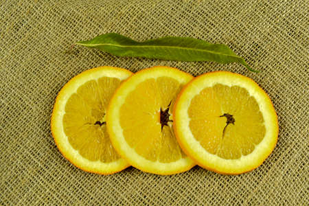 Slices of orange with green leaves on a burlap backgroundの写真素材