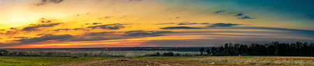 the colorful sunset over the fields with the village visible in the backgroundの写真素材