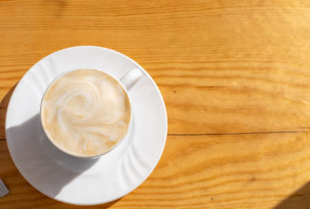 white coffee in a cup on a brown tableの写真素材